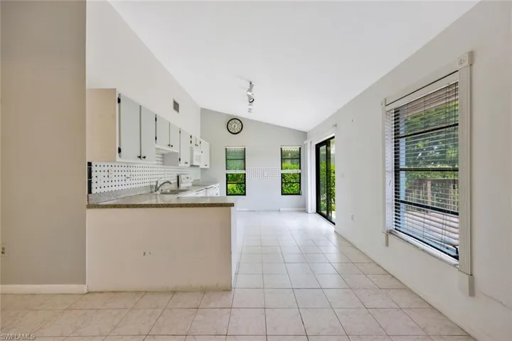 Kitchen with white cabinets, light tile patterned floors, sink, lofted ceiling, and tasteful backsplash