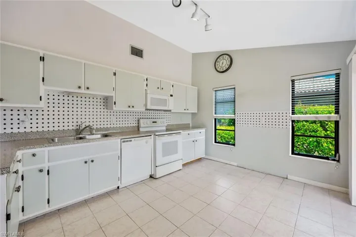 Kitchen featuring vaulted ceiling, white appliances, white cabinetry, sink, and track lighting
