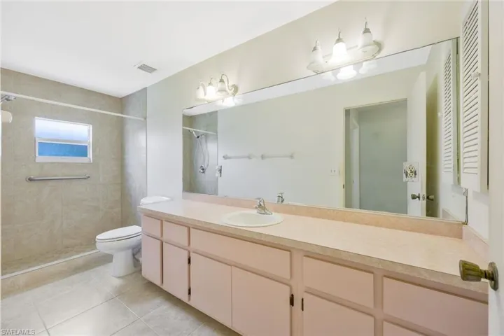 Bathroom featuring tiled shower, vanity, toilet, and tile patterned flooring