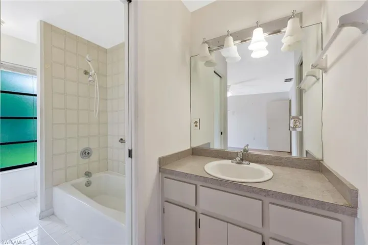 Bathroom featuring tile patterned flooring, a healthy amount of sunlight, tiled shower / bath, and vanity