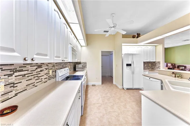 Kitchen with sink, light tile patterned floors, tasteful backsplash, white appliances, and white cabinets