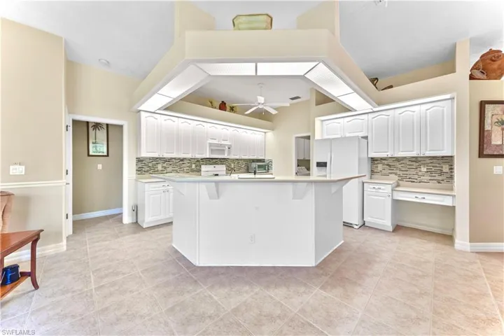 Kitchen with white cabinets, white appliances, and a kitchen island with sink