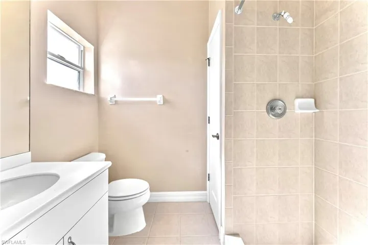 Bathroom featuring tile patterned flooring, vanity, toilet, and a tile shower
