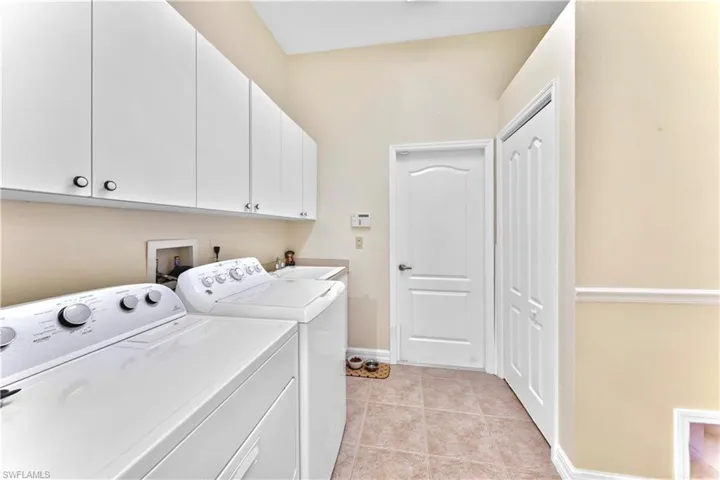 Laundry area with light tile patterned flooring, cabinets, sink, and washing machine and dryer