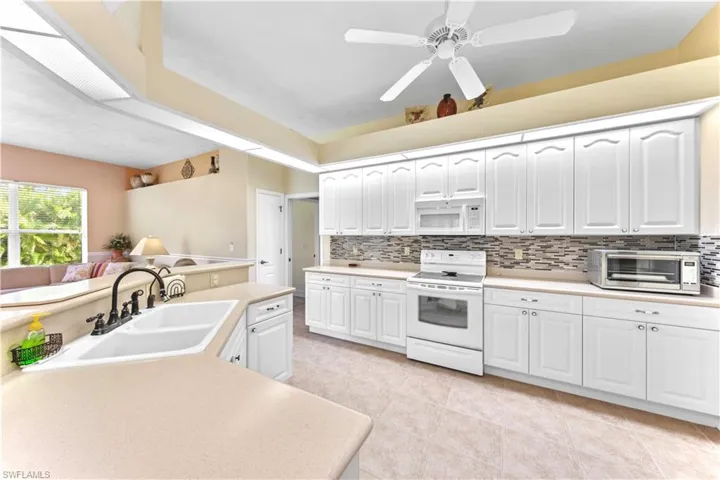 Kitchen with white appliances, ceiling fan, sink, light tile patterned floors, and white cabinets