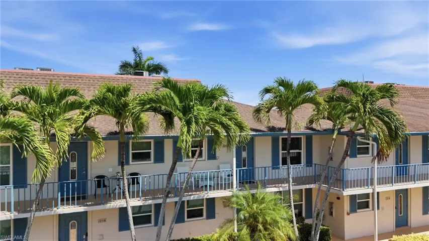 Multi-level building with individual entrances, balconies with blue railings, and abundant palm trees