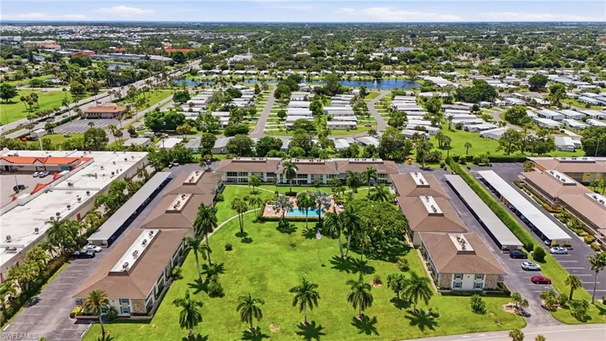 Community setting featuring multiple residential buildings, a central green space, a swimming pool, and covered parking structures