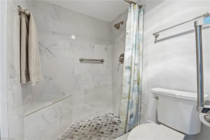 Shower with white marble-look tile, built-in corner bench, and mosaic tile flooring