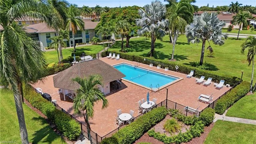 Outdoor swimming pool with a surrounding paver deck, a shaded cabana structure, and an adjacent green space