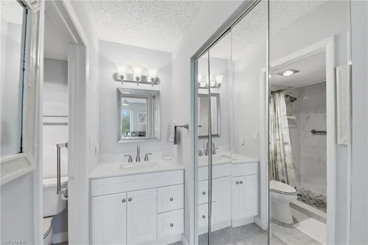 Dual vanities with white cabinetry, mirrored closet doors, and separate shower and commode areas