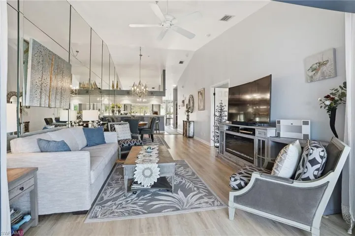 Living area featuring suspended lighting, light wood finished floors, a ceiling fan, and vaulted ceiling