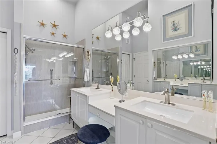 Full bathroom featuring two vanities, a stall shower, light tile patterned floors, and a high ceiling