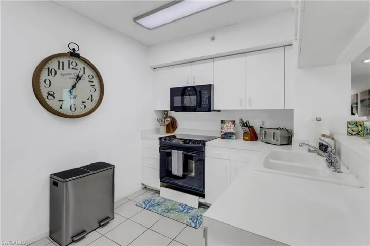 Kitchen featuring light countertops, black appliances, white cabinets, and light tile patterned floors