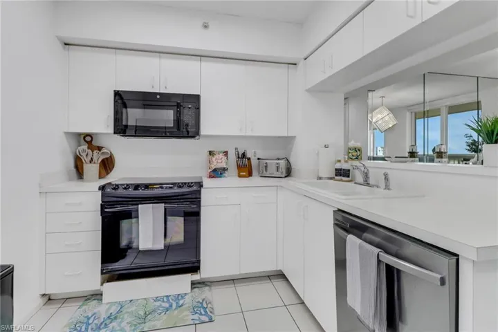 Kitchen featuring black appliances, light countertops, white cabinets, light tile patterned floors, and a peninsula