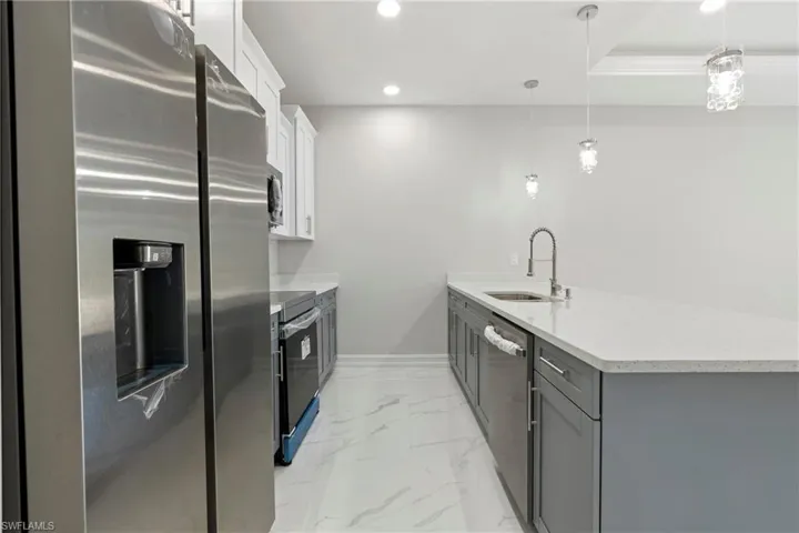 Kitchen featuring a peninsula, marble finish floor, stainless steel appliances, gray cabinetry, and a sink