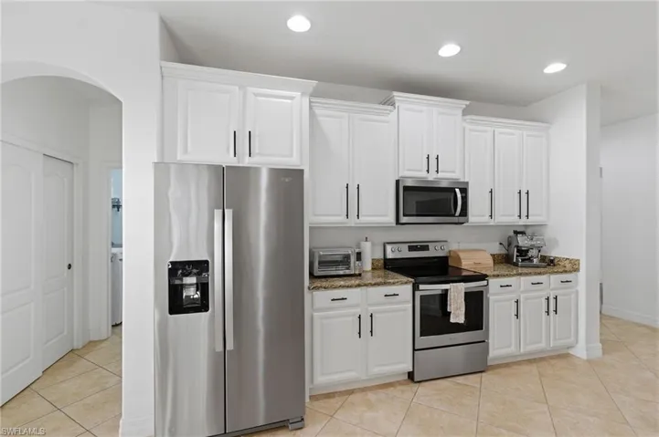 Kitchen featuring stainless steel appliances, light stone counters, white cabinetry, light tile patterned floors, and recessed lighting