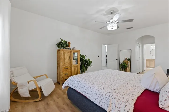 Bedroom featuring wood finished floors, arched walkways, ensuite bathroom, and ceiling fan