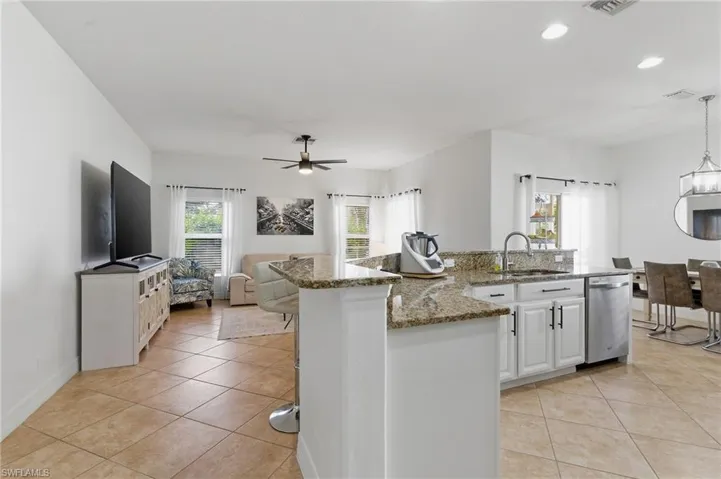 Kitchen with white cabinets, light stone counters, an island with sink, and light tile patterned floors