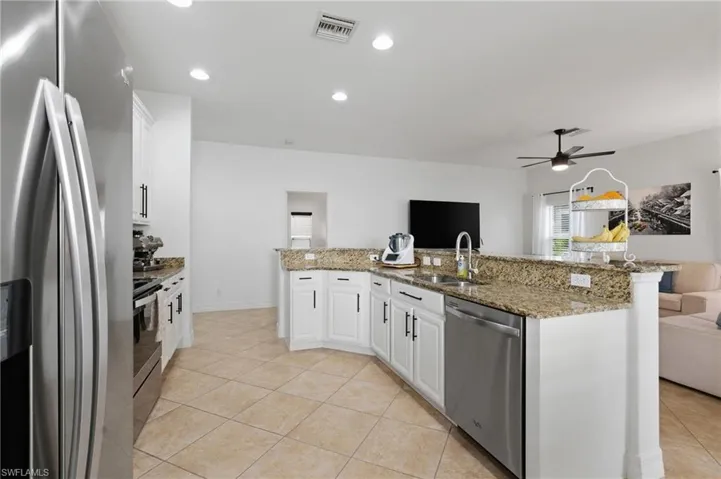 Kitchen featuring stainless steel appliances, white cabinetry, open floor plan, light stone countertops, and light tile patterned floors