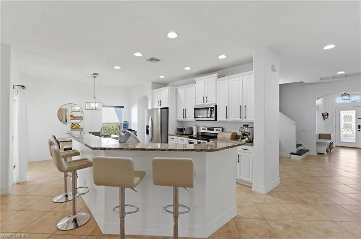 Kitchen with arched walkways, white cabinetry, dark stone counters, decorative light fixtures, and a kitchen breakfast bar