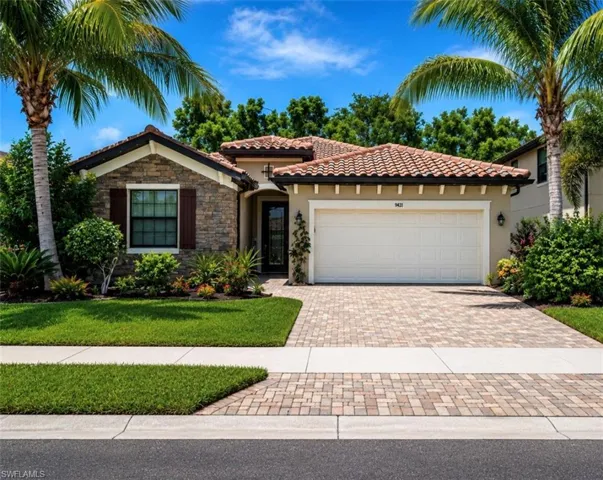 Stucco and stone facade home featuring a tile roof, an integrated garage, a paver driveway, and mature palm trees