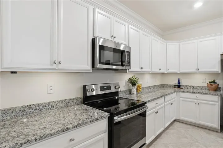 Kitchen with stainless steel appliances, ornamental molding, light stone countertops, and white cabinets