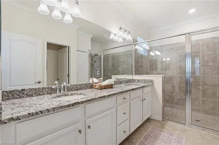 Full bathroom with double vanity, a stall shower, crown molding, suspended lighting, and light tile patterned floors