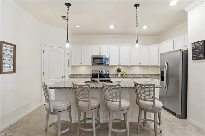 Kitchen with stainless steel appliances, white cabinetry, a center island with sink, light stone counters, and ornamental molding