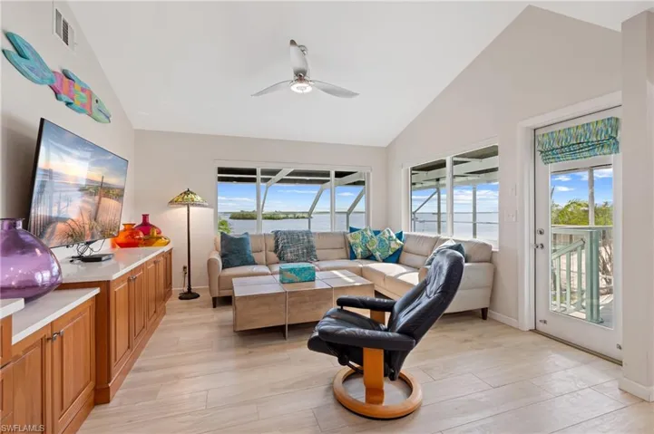 Living room with light hardwood / wood-style flooring, high vaulted ceiling, ceiling fan, and a water view / virtually enhanced