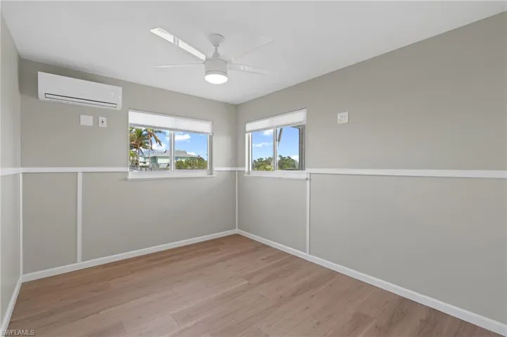Empty room featuring ceiling fan, light hardwood / wood-style floors, and a wall mounted AC /  virtually enhanced photo