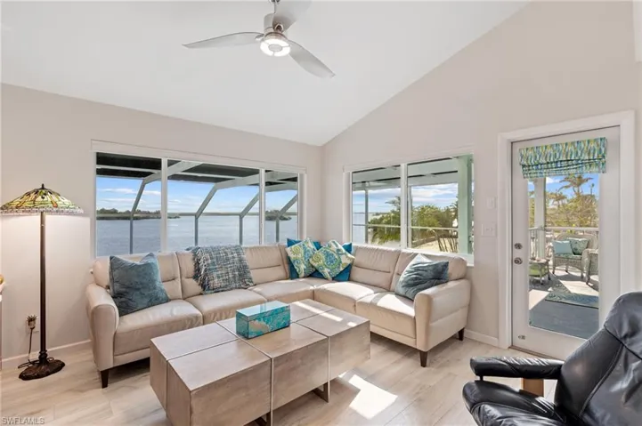 Living room with light hardwood / wood-style flooring, high vaulted ceiling, ceiling fan, and a water view / virtually enhanced