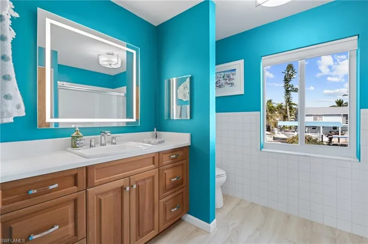 Bathroom with a shower with door, vanity, tile walls, and toilet /  virtually enhanced photo