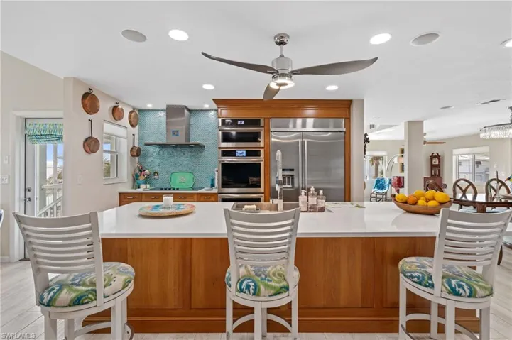 Kitchen featuring wall chimney range hood, ceiling fan, stainless steel appliances, a spacious island, and tasteful backsplash / virtually enhanced