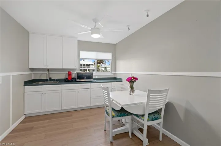 Kitchen with white cabinetry, ceiling fan, sink, and light hardwood / wood-style flooring /  virtually enhanced photo