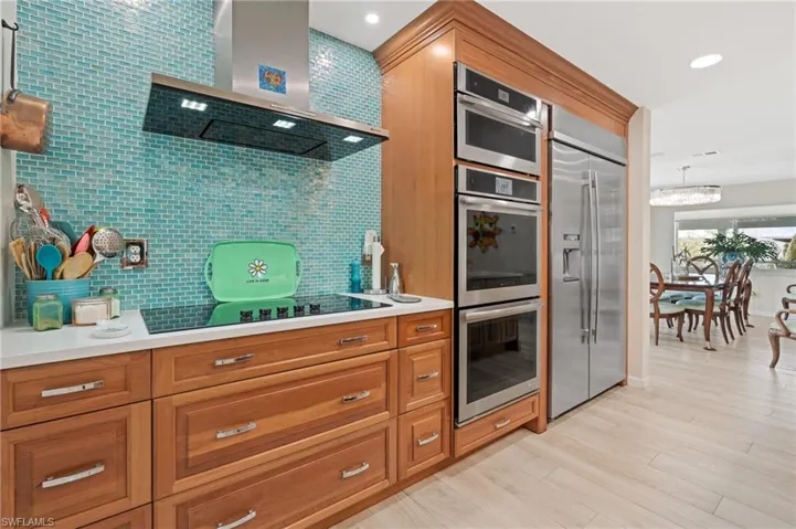 Kitchen featuring tasteful backsplash, decorative light fixtures, light hardwood / wood-style flooring, stainless steel appliances, and wall chimney range hood / virtually enhanced