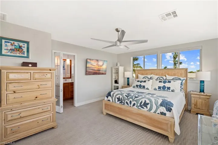Bedroom featuring ceiling fan, light colored carpet, and ensuite bath / virtually enhanced