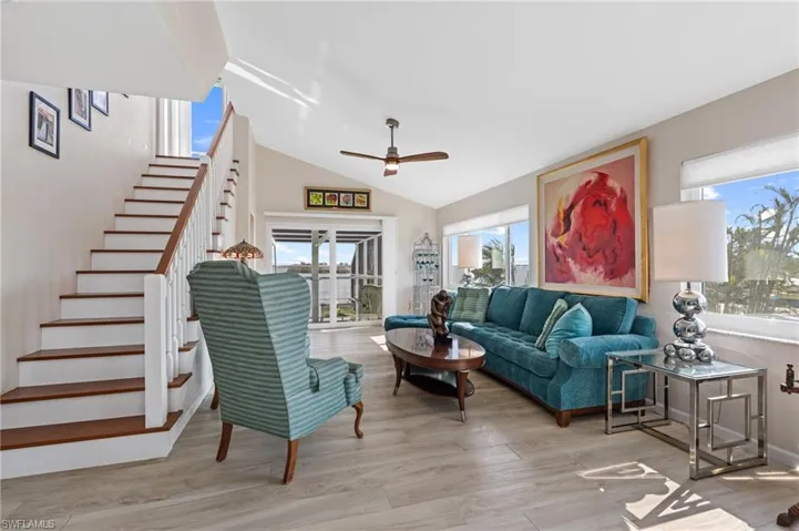Living room with light hardwood / wood-style flooring, ceiling fan, and vaulted ceiling / virtually enhanced