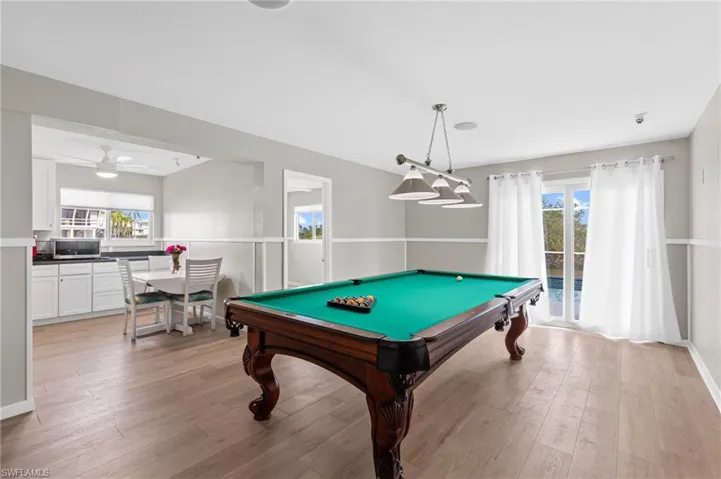 Game room with ceiling fan, billiards, and light wood-type flooring /  virtually enhanced photo