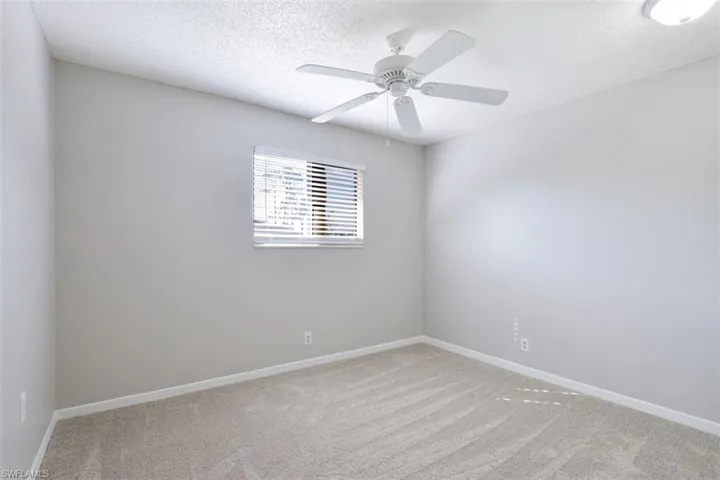 Empty room featuring a textured ceiling, light carpet, and ceiling fan