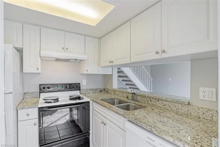 Kitchen with sink, white appliances, light stone counters, and white cabinets