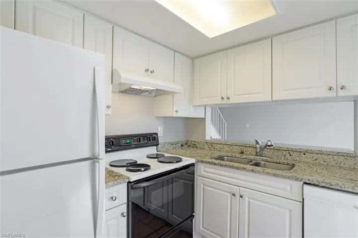 Kitchen with sink, white appliances, light stone counters, and white cabinets