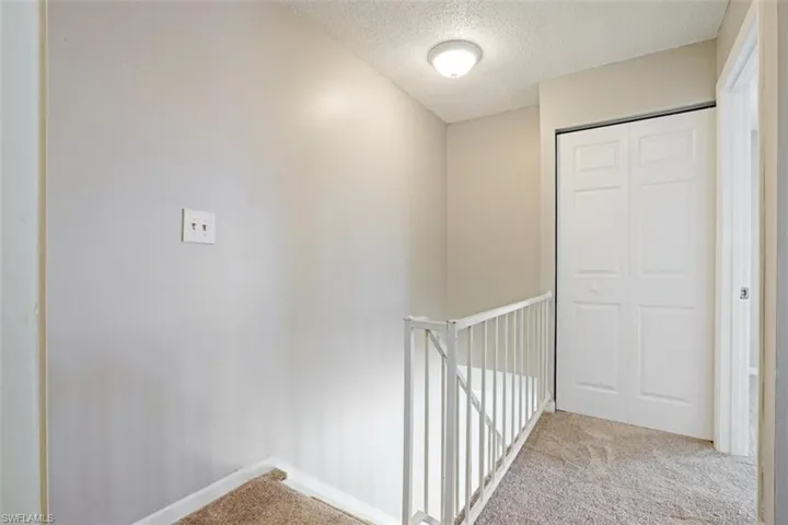 Hallway featuring a textured ceiling and light colored carpet
