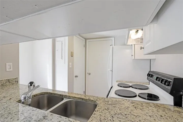 Kitchen featuring range with electric cooktop, sink, light stone countertops, and white cabinetry