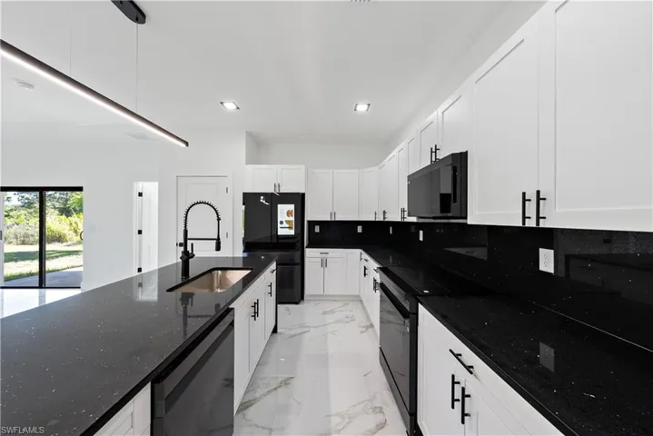 Kitchen featuring white cabinets, black appliances, dark stone countertops, marble finish floor, and a sink