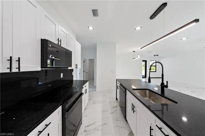 Kitchen with baseboards, black microwave, visible vents, marble finish floor, and a sink