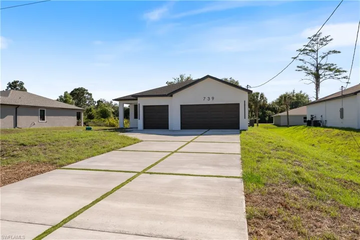 View of front of house featuring an outbuilding, concrete driveway, stucco siding, and a front lawn