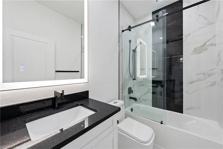 Bathroom with toilet, vanity, and bath / shower combo with glass door
