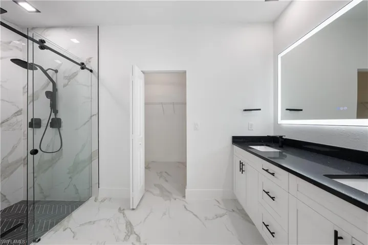 Bathroom with baseboards, a spacious closet, a marble finish shower, marble finish floor, and a sink