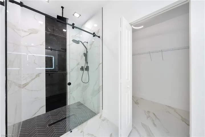 Bathroom featuring a walk in closet, marble finish floor, baseboards, and a marble finish shower