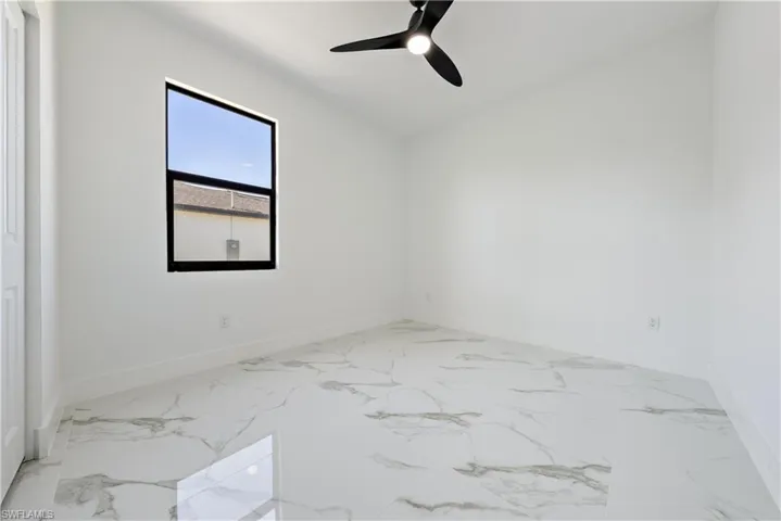 Empty room featuring marble finish floor, ceiling fan, and baseboards